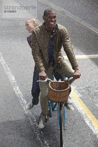 Glückliches Paar beim Radfahren in der verregneten Straße