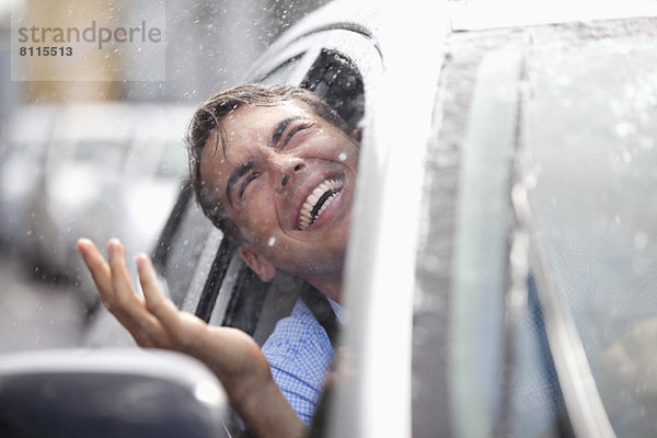 Enthusiastischer Mann im Auto mit Blick aus dem Fenster auf Regen