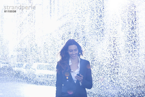 Glückliche Geschäftsfrau SMS mit Handy im Regen