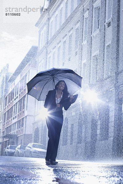 Geschäftsfrau steht unter dem Regenschirm in der verregneten Straße