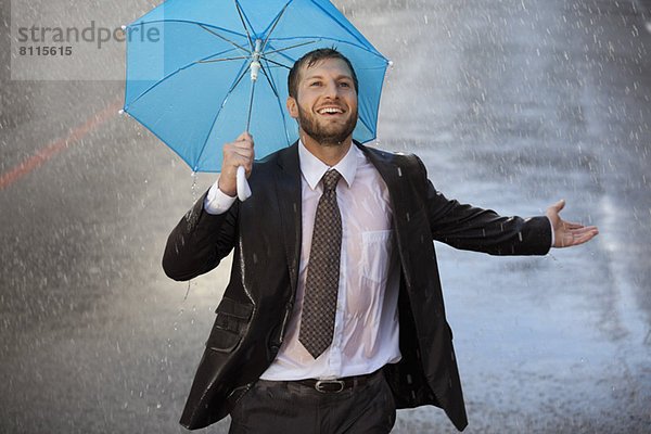 Enthusiastischer Geschäftsmann mit winzigem Regenschirm in verregneter Straße