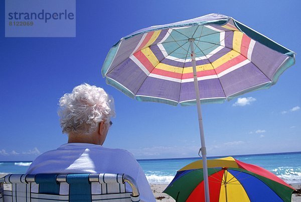 Rückansicht  Halbportrait  Außenaufnahme  Senior  Senioren  Seniorin  Einzelperson  eine Person  Europäer  Farbaufnahme  Farbe  Urlaub  Vereinigte Staaten von Amerika  USA  Tag  Entspannung  1  ruhen  Strand  Regenschirm  Schirm  Reise  Querformat  Nordamerika  Staatsbürger  Sonnenschirm  Schirm  Florida  freie Natur