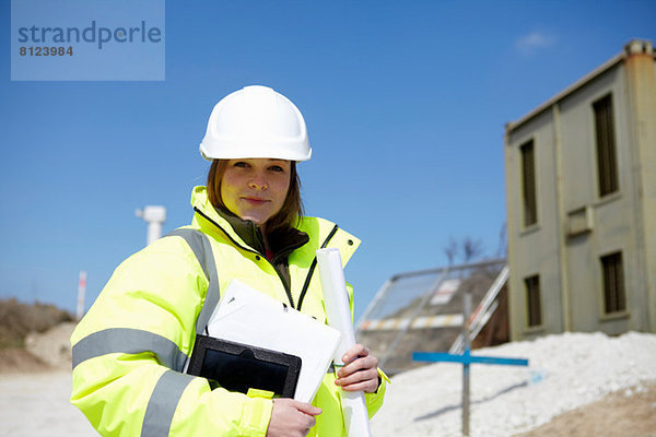 Porträt einer Frau mit Bauplan und digitalem Tablett auf der Baustelle