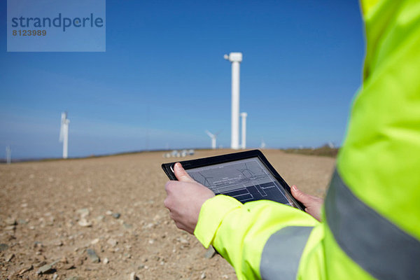 Projektleiter mit digitalem Tablett vor dem Windpark