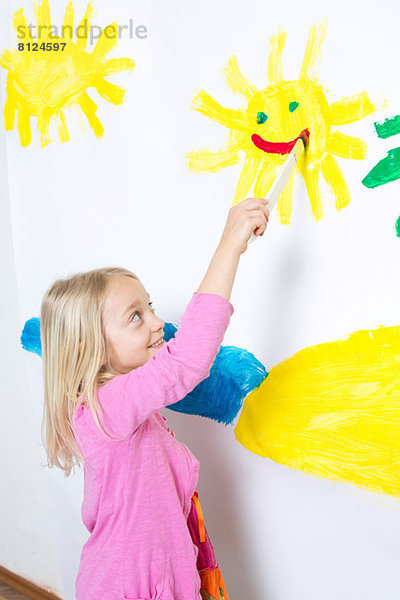 Junges Mädchen malt lächelnden Sonnenschein an die Wand