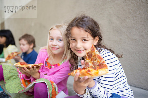 Kleine Gruppe von Kindern beim Pizzaessen im Freien