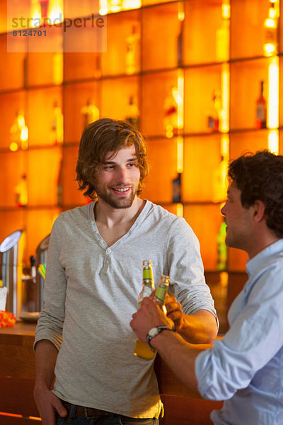 Zwei Männer stehen an der Bar mit Bierflaschen.