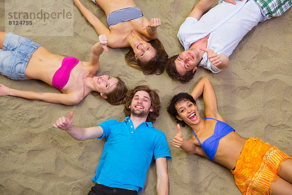 Luftaufnahme von Freunden  die mit Köpfen zusammen auf Sand liegen