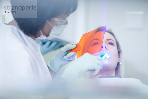 Zahnärztin mit ultraviolettem Licht an den Zähnen des Patienten