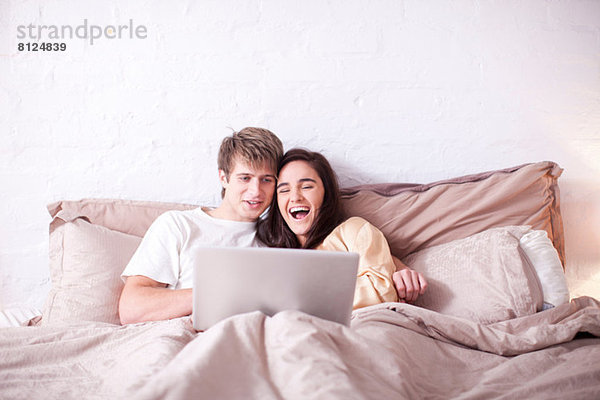 Junges Paar beobachtet Laptop im Bett