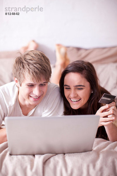 Junges Paar auf dem Bett liegend mit Blick auf den Laptop