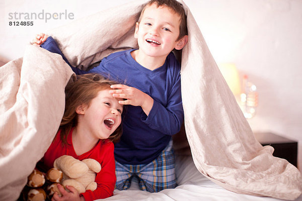Zwei kleine Kinder spielen unter der Bettdecke