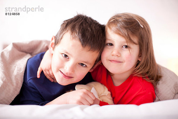Zwei kleine Kinder  die sich unter der Bettdecke umarmen.