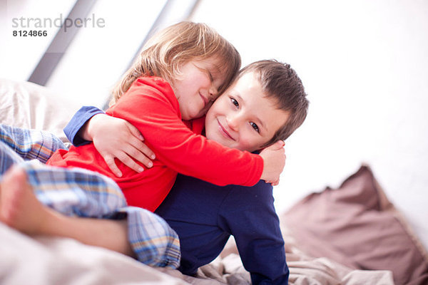 Zwei kleine Kinder  die sich auf dem Bett umarmen.