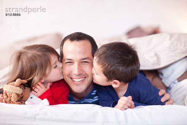 Sohn und Tochter küssen Väter Wange unter Bettdecke