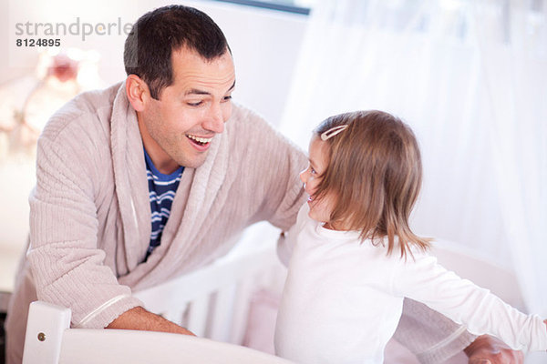 Vater spielt mit kleiner Tochter im Kinderbett