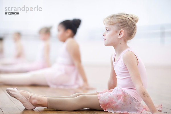 Junge Ballerinas in Pose auf dem Boden sitzend