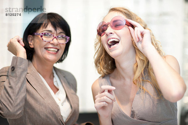 Zwei Frauen lachen  während sie eine Brille anprobieren.