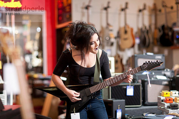 Junge Frau spielt E-Gitarre im Musikladen
