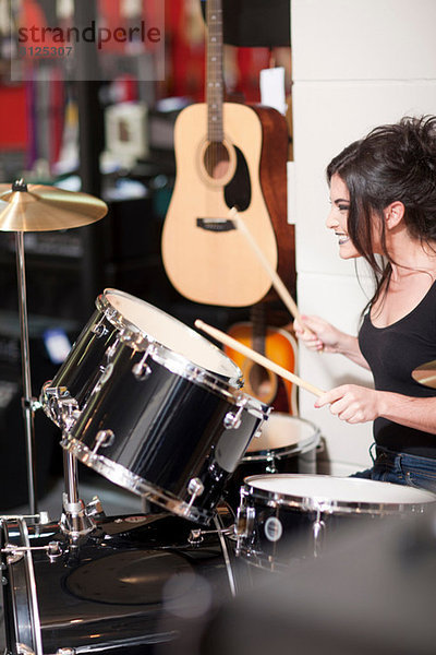 Junge Frau probiert Schlagzeug im Musikladen aus