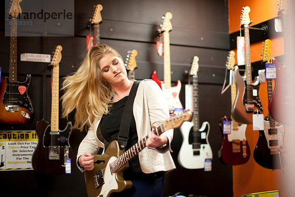 Junge Frau testet Gitarre im Musikladen