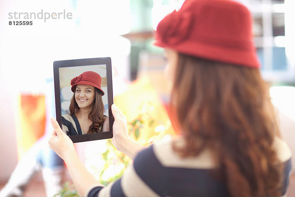 Frau mit bordeauxfarbenem Hut nimmt Selbstporträt auf digitalem Tablett auf