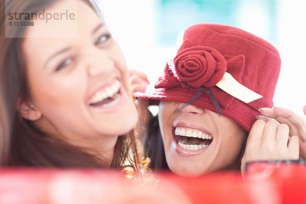 Zwei Freundinnen  die mit einem burgunderroten Hut herumspielen.