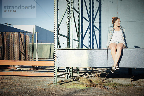 Frau sitzt an der Wand im Industriegebiet