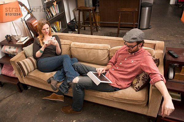 Paar auf dem Sofa sitzend mit digitalem Tablett und Smartphone