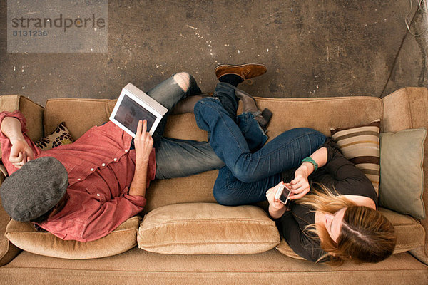 Paar auf dem Sofa sitzend mit digitalem Tablett und Smartphone