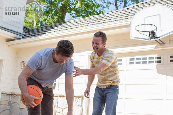 Vater hält Basketball mit erwachsenem Sohn lacht