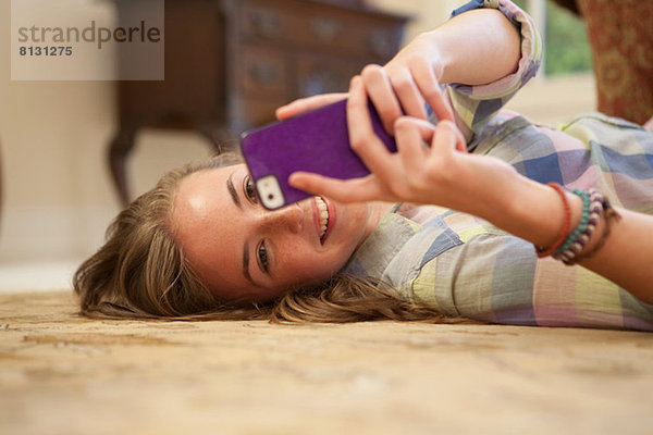 Teenagermädchen auf dem Boden liegend mit Handy