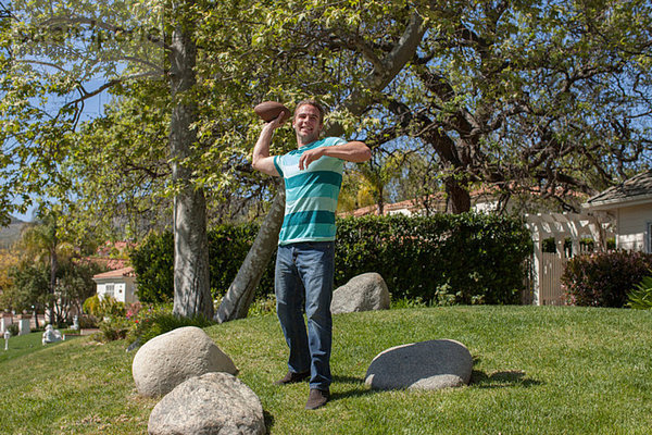 Junger Mann wirft American Football in den Garten