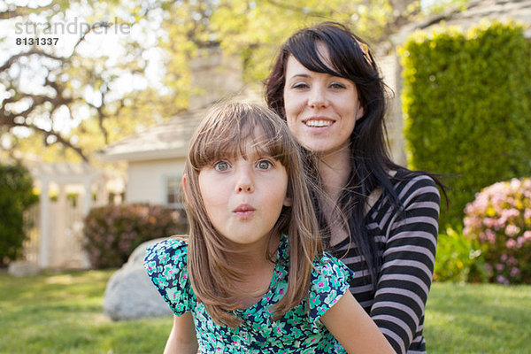 Porträt von Mutter und Tochter  die im Garten das Gesicht ziehen