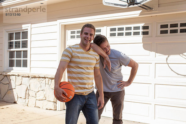 Vater stützt sich auf die Schulter des erwachsenen Sohnes mit Basketball