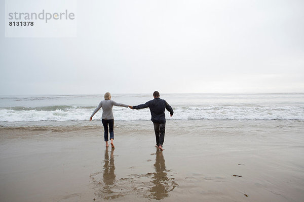 Ein reifes Paar hält sich am Strand an den Händen.