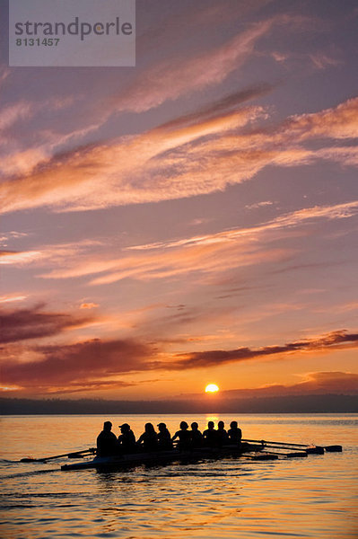 Acht Personen rudern bei Sonnenuntergang