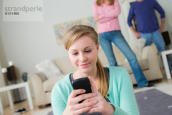 Teenager-Mädchen benutzt Handy  Eltern im Hintergrund