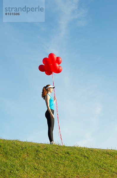 Teenagermädchen steht auf Gras und hält rote Luftballons.