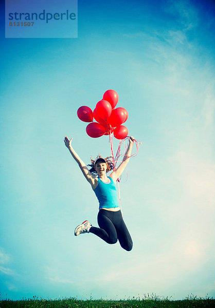 Teenager-Mädchen springt in der Luft und hält rote Luftballons.