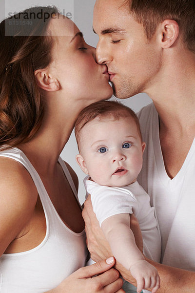 Mutter und Vater küssen sich  mit Baby-Tochter