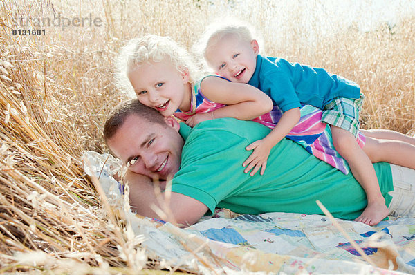 Vater mit Sohn und Tochter auf dem Feld übereinander liegend