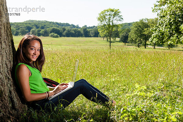 Junge Frau mit Laptop am Baum sitzend