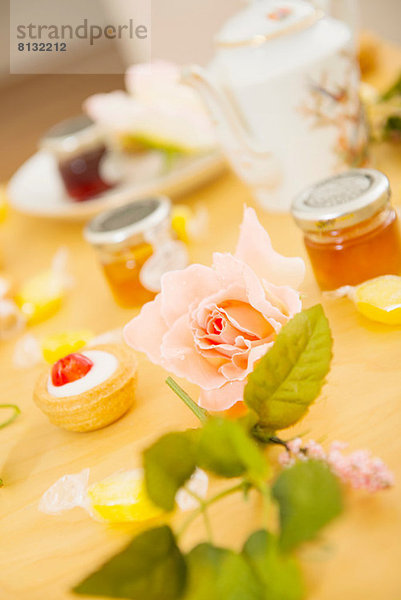 Rose auf dem Tisch mit Teegetränken und Süßigkeiten