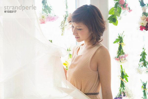 Frau hebt Vorhänge von Glasfenstern mit baumelnden Blumen an