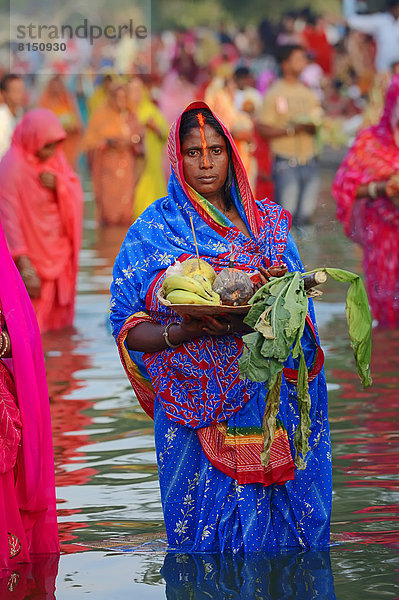 Frau in blauen Sari gekleidet mit Opfergaben steht im Wasser beim hinduistischen Chhath-Fest oder Chhath-Festival