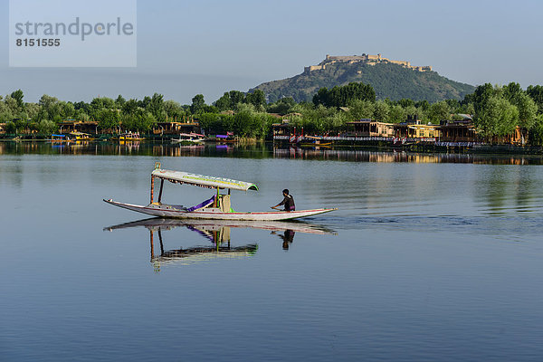 Ein Shikara-Boot überquert den Dal Lake oder Dal-See  Hausboote und das Durrani Fort auf dem Hari Parbat Hügel hinten