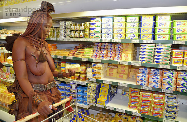 Traditionell gekleidete Himba-Frau vor dem Kühlregal im Supermarkt mit Butter in der Hand