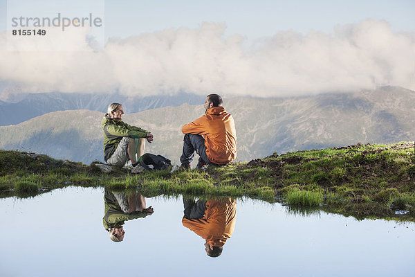 Zwei Wanderer spiegeln sich in einem kleinen Bergsee