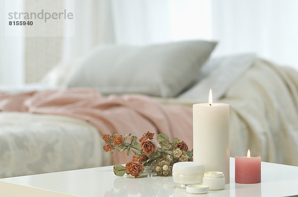Kerzen  Hautcreme und Rosenstrauß auf Tisch mit Bett im Hintergrund